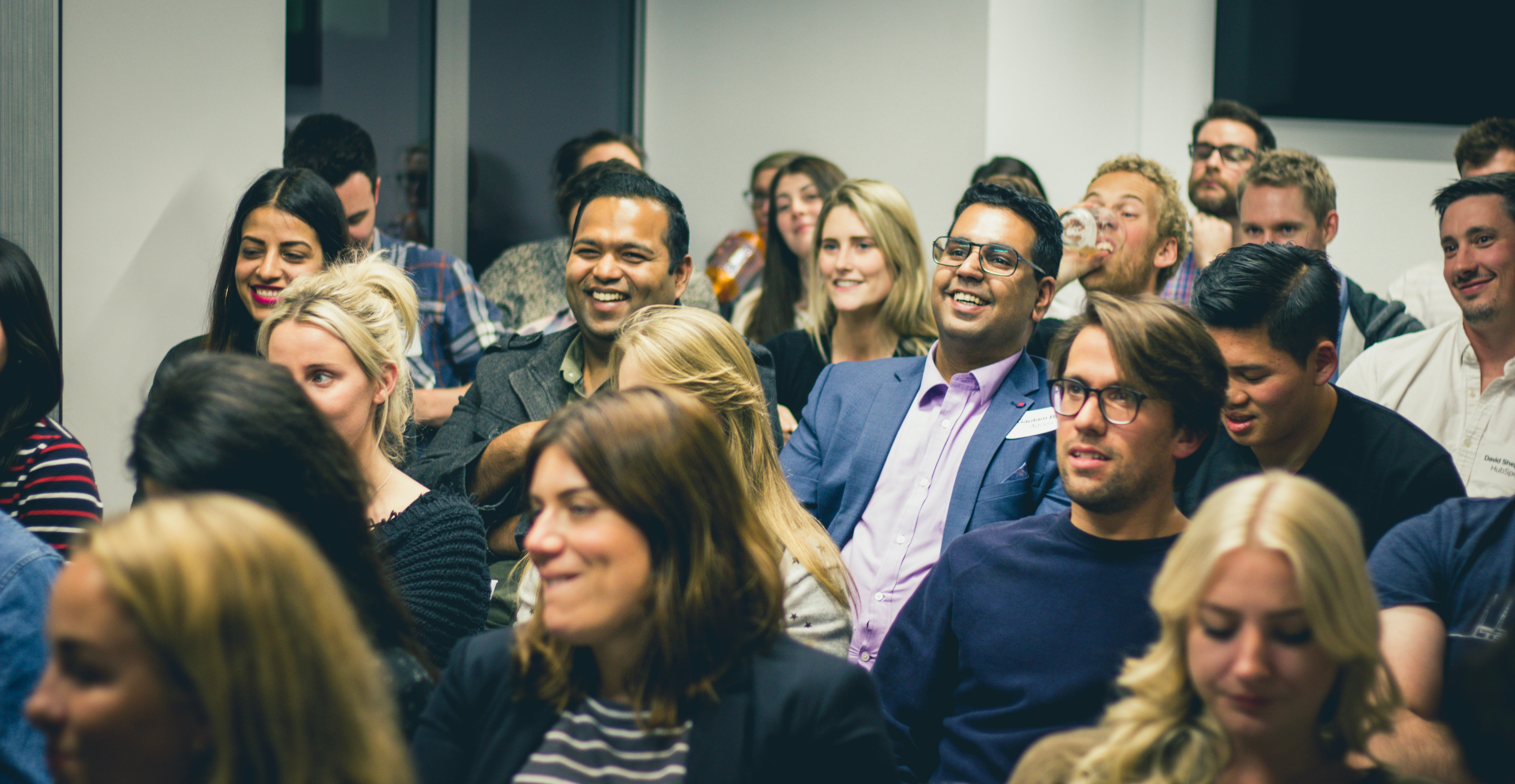 groupof people sitting in an audience and laughing, smiling, and engaging with the speaker. 
